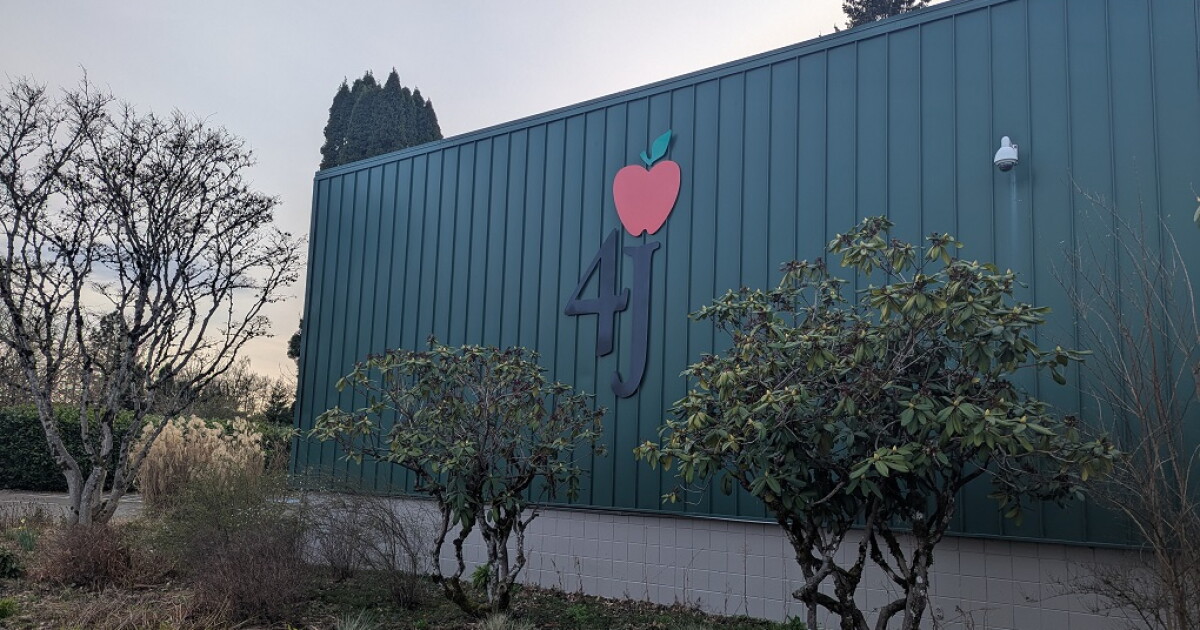 Green outdoor wall with 4J and an apple logo on it. in the foreground bushes and a sidewalk.