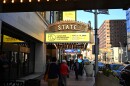 People walk down a sidewalk under a theater marquee sign