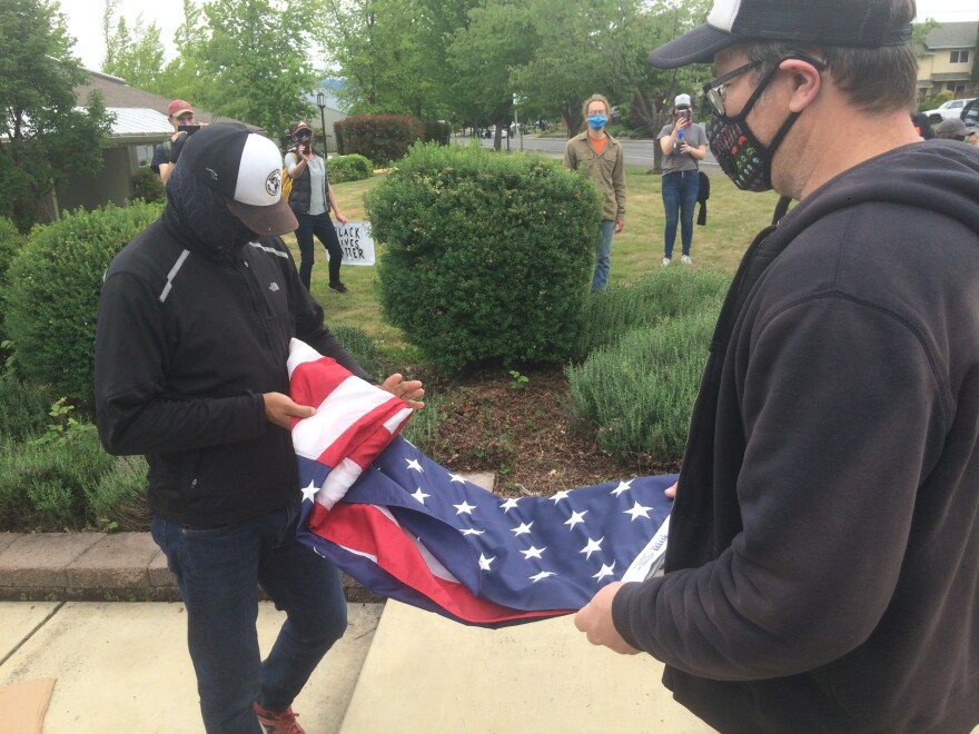 Two demonstrators fold an American flag that was pulled down from the flag pole in front of the Ashland Police headquarters on Sunday, May 31, 2020. The flag was later returned.