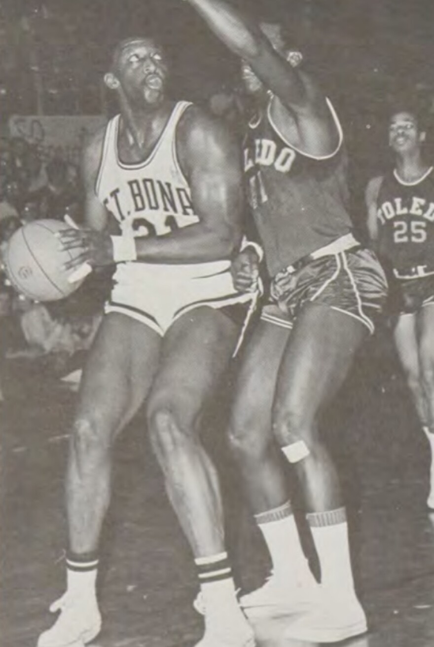 Bob Lanier, on the left wearing a white uniform, holds a basketball ready to take a shot.