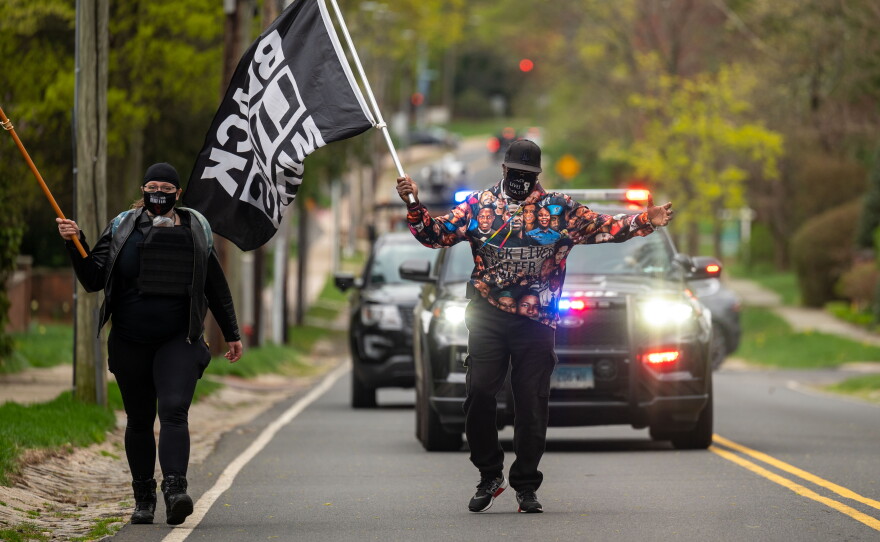 A man walking in the middle of the road during a Black Lives Matter Protest with a cop car behind him.