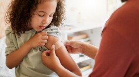 A child looks at her left arm as a medical professional smooths out a bandage