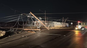 A broken electric pole and wires dangle over an intersection in Grand Blanc. The sky is dark and a part of firetruck is visible in the image. 