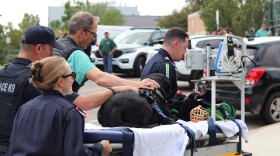 Veterinarians and Police officers push a stretcher toward the hospital door. On the stretcher lays a black Labrador.