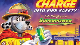 Cartoon image of Sparky, the National Fire Prevention Association's mascot, holding a cell phone charger and a battery - a campaign image for "Charge into Fire Safety - Safe Charging is a Superpower."