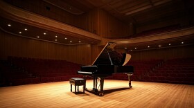 A black grand piano sits on an empty stage.