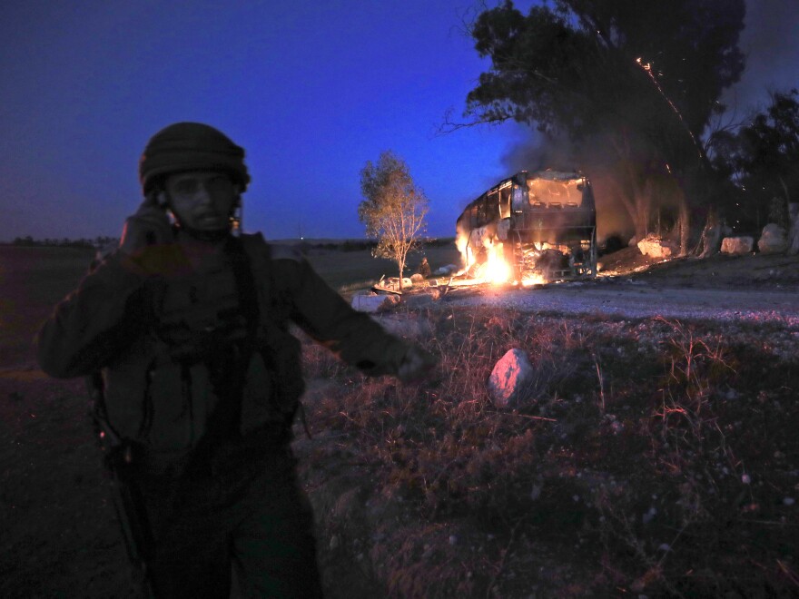 An Israeli soldier stands near a burning bus that was hit by a mortar shell fired from Gaza on Monday.