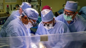 Surgeons hover over a patient in an operating room.