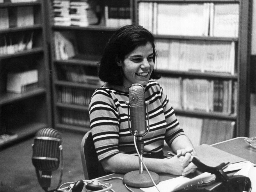 Susan Stamberg at a microphone, age 25. Later, as the host of All Things Considered, she was the first woman to be a full-time anchor of a U.S. national nightly news broadcast.