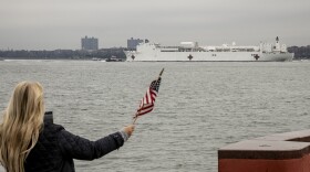 The U.S. Navy hospital ship Comfort is welcomed to New York City by Charlene Nickloan, waving a flag from the Matthew Buono war memorial in Staten Island, N.Y., on Monday.