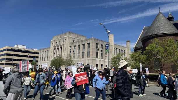 A photo of people carrying signs walking in downtown Greensboro for the city's third No Kings protest.