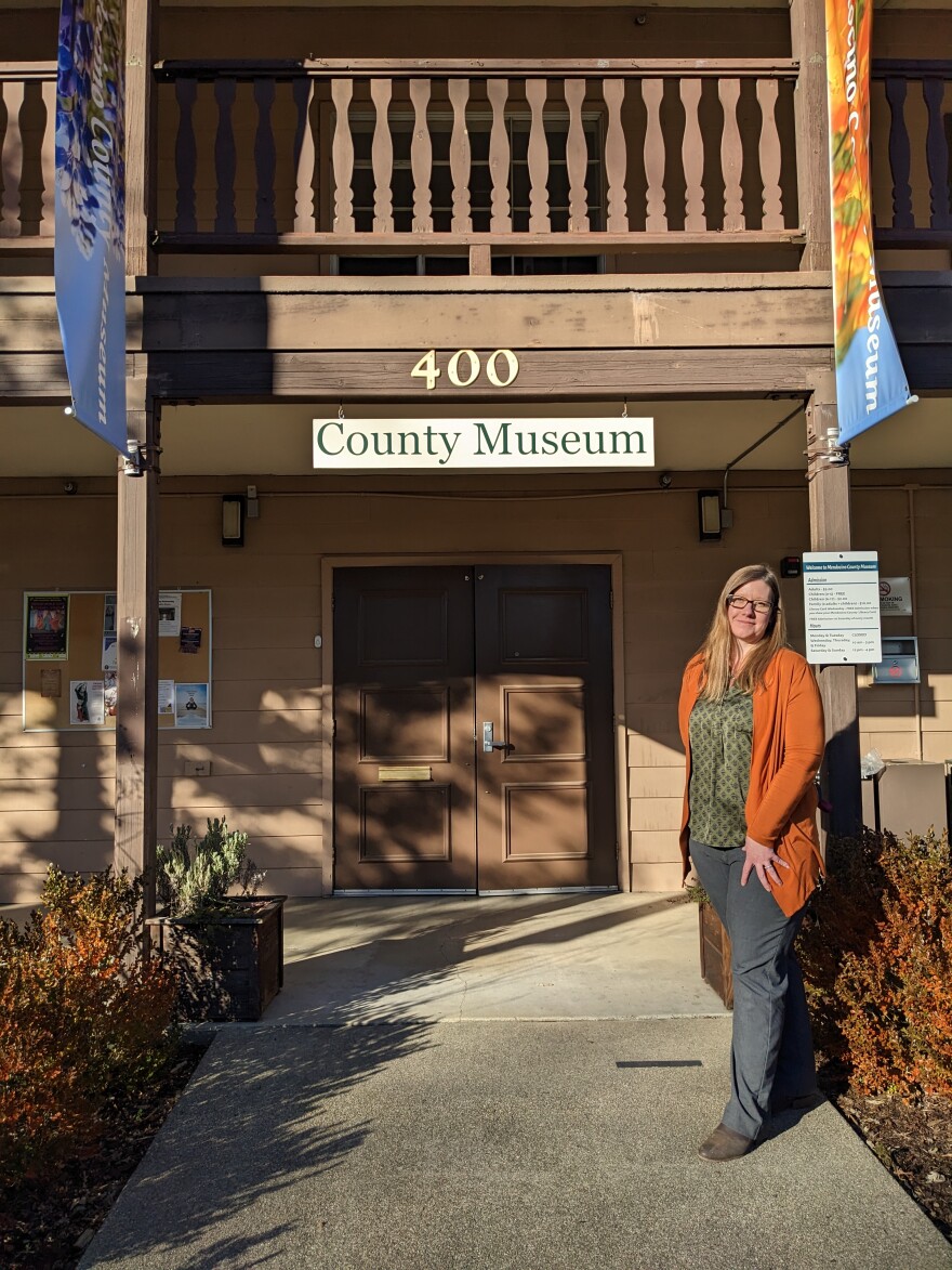 A woman stands outside a building with wooden double doors and a sign that says, "County Museum."