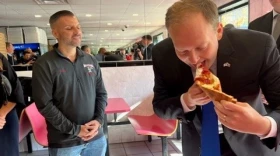 Long Island Rep. Lee Zeldin, who's the Republican candidate for New York governor, takes a bite of the chicken parm pizza at Paesan's Pizza that was his favorite when he was a student at the State University of New York at Albany. Owner Frank Scavio is at left. (Karen DeWitt / New York State Public Radio)