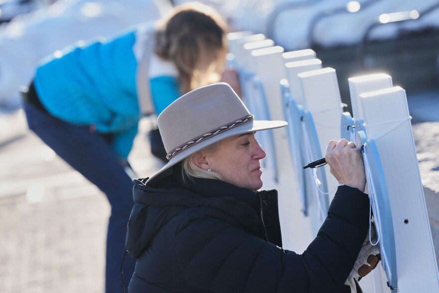 A closeup of a woman writing on a wooden heart-shaped sign at a vigil.
