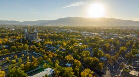 Aerial photo of Logan City in the daytime, with buildings, trees, the Logan LDS Temple, and mountains all in view.