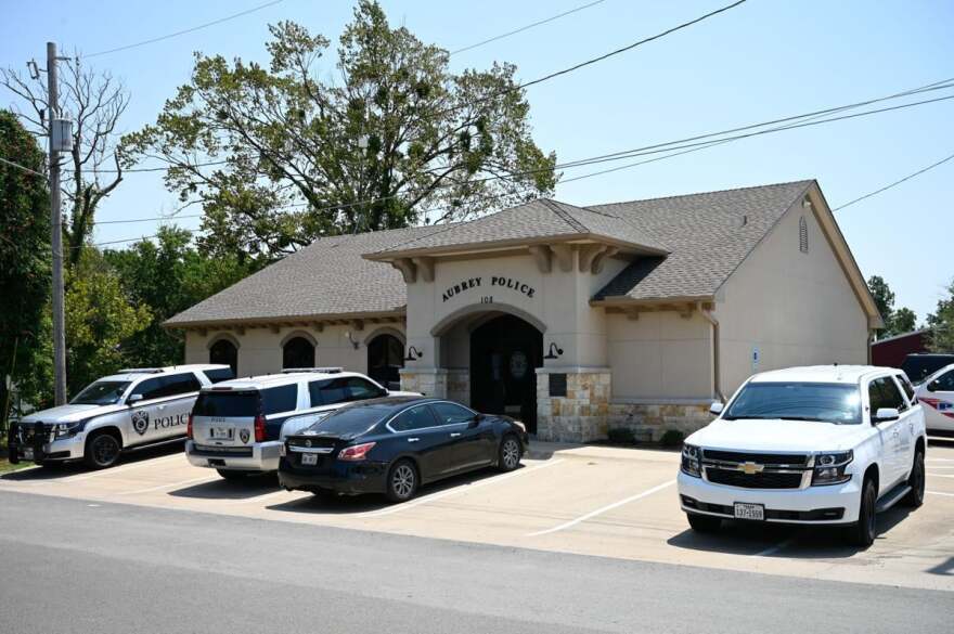 Four vehicles parked in front of a one-story building that says “Aubrey Police”