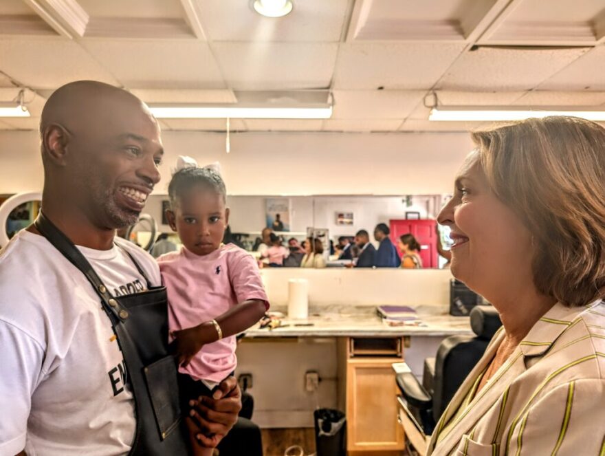Antonio Brown (left), owner of Central Station Barbershop and Grooming, holds his daughter, Jazelle, while speaking to Congresswoman Kathy Castor.