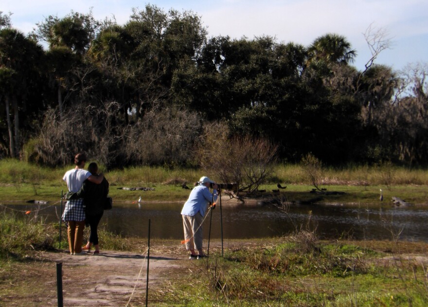 Two people arm-in-arm at a state park while a person to the right takes pictures on a tripod