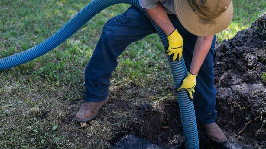 Jeremy Langford, an employee at AA ARON Super Rooter, center, cleans out a septic tank at a home in Miami, Florida on Wednesday, September 30, 2020.