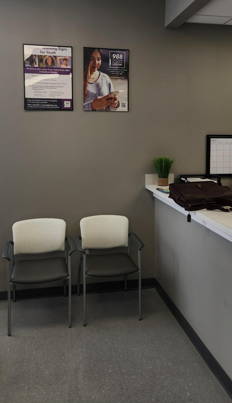 Two 988 suicide prevention posters hang on the wall above two chairs in the clinic waiting room