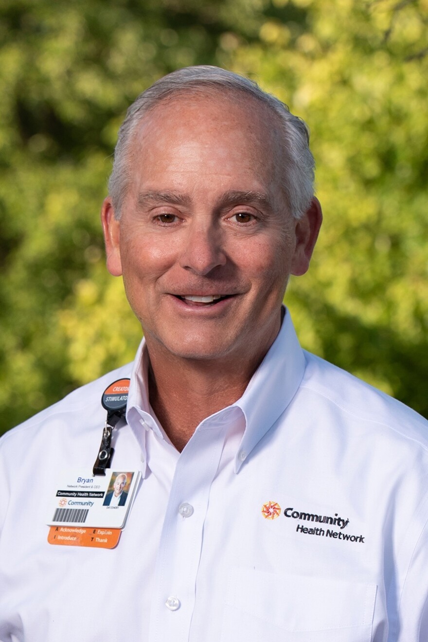 Man with grey hair smiles at the camera with mouth slightly open. He is wearing a white shirt with a logo that reds Community Health Network.