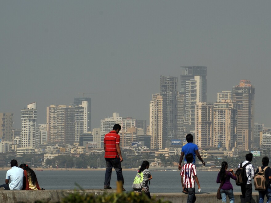 The Mumbai city skyline is seen in the background as pedestrians walk and gather on the seaside promenade in Mumbai on January 12, 2012