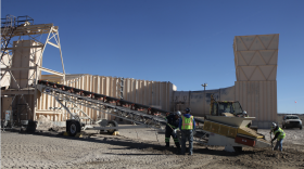 Workers in high-visibility vests use shovels to dig around a large mechanical structure
