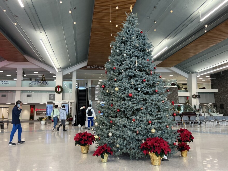  A decorated Christmas tree with red and gold ornaments sits in front of two escalators. 