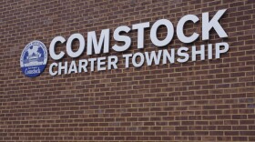 On a brick wall, a sign reads "Comstock Charter Township" and is depicted with the township seal next to it. 