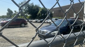 Cars sit behind a chain-link fence in a tow lot.
