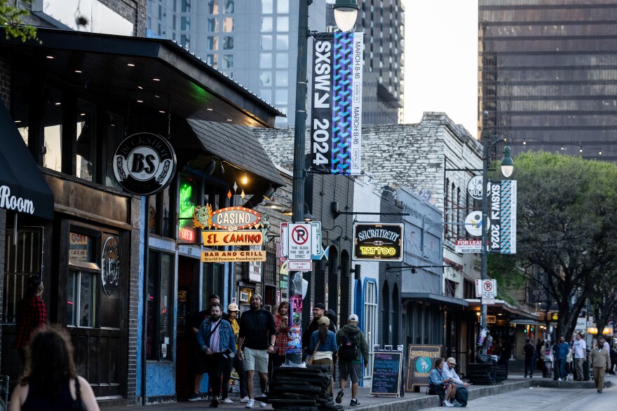 Pedestrians walk along Sixth Street under SXSW banners.