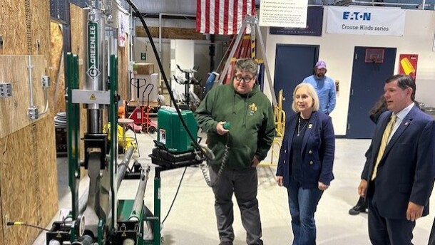 Senator Kirsten Gillibrand and two union members in warehouse with conduit-bending machine. 