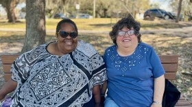 Two older women, Mary Jones and Carita Wells, sit on a park bench in Tampa