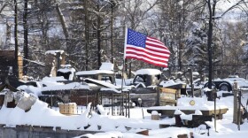 An American flag flutters in the wind over the charred remains of vehicles and a home destroyed by wildfires Thursday, Jan. 6, 2022, in Superior, Colo. (AP Photo/David Zalubowski)
