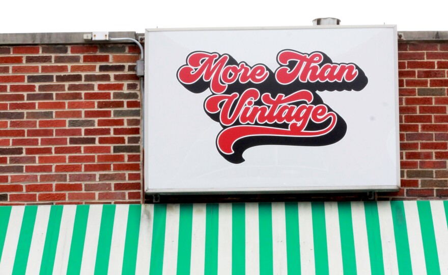 Image of More Than Vintage, a vintage store in downtown East Lansing. The building is brick. There's a green and white-striped awning that hangs over the shop door. The sign reads "More than vintage" in a 70s era font.