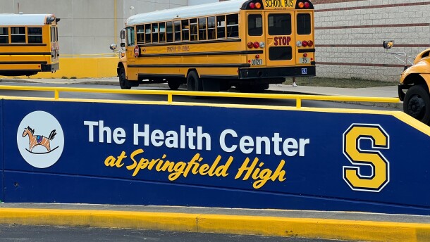A sign announces the Health Center at Springfield High. Yellow school buses line up behind it.