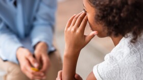 Close up view of african american girl with hand near eye crying during consultation with blurred psychologist on background