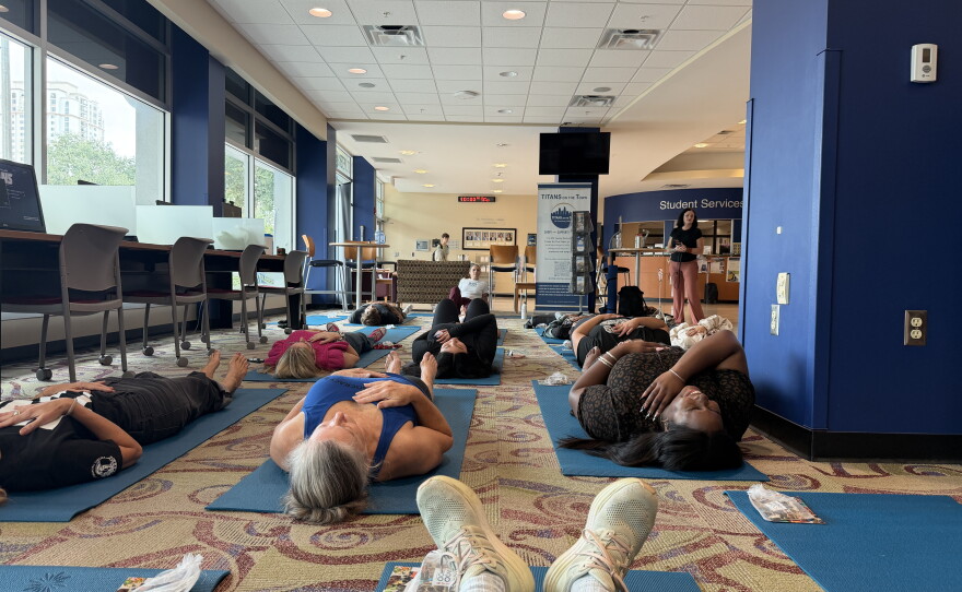 People on the ground are lined up on blue yoga mats doing yoga poses. 