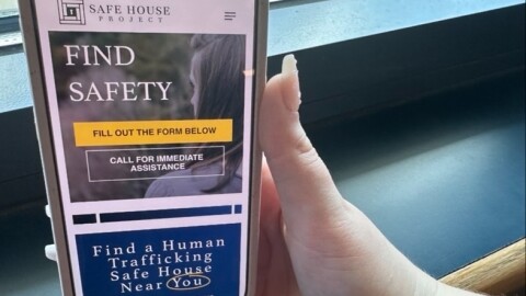 A hand holding a phone that shows the Simply Report app on it.