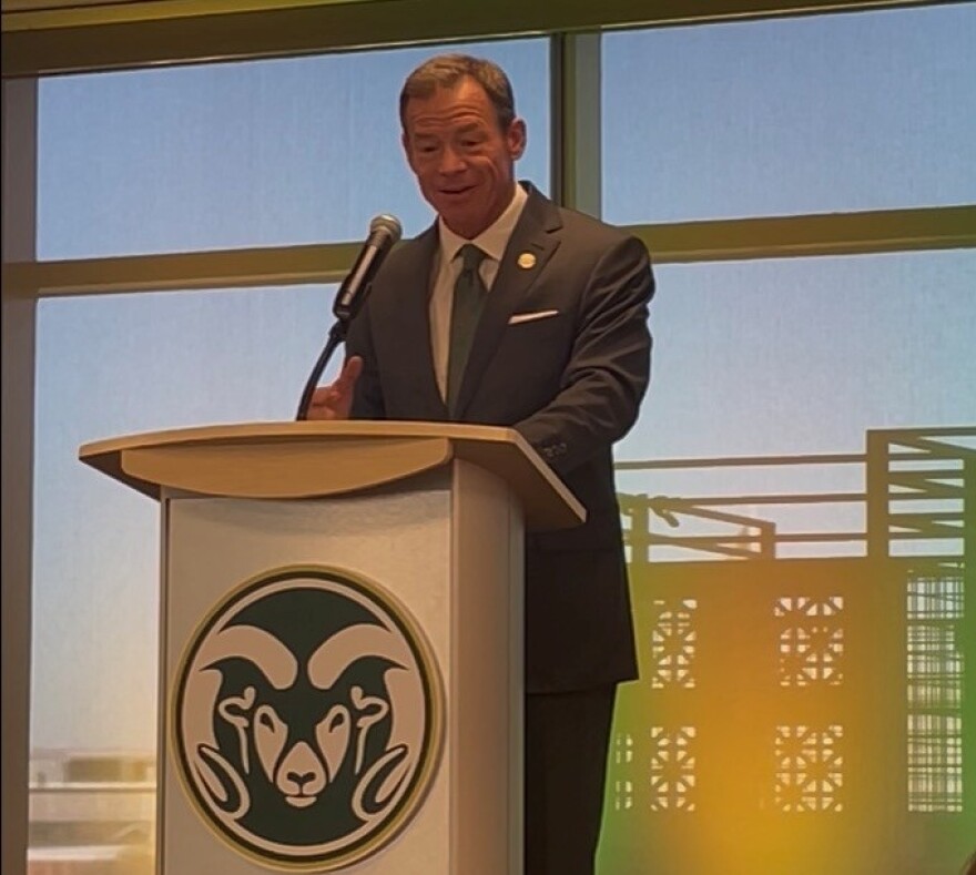 A man stands and speaks from a podium at a conference setting. 