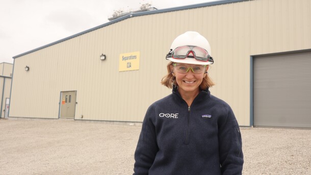 Director of Technology and Sustainability Andrea Vanderhoff wears a hard hat and branded zip-up and stands in front of QORE's separations building.