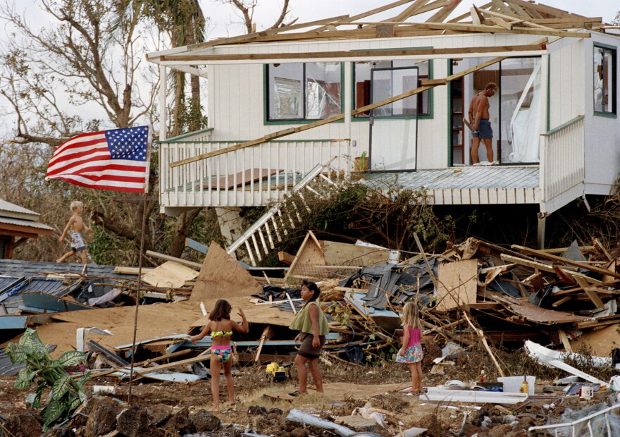 An American flag waves in the wind while debris from homes is seen along the beach