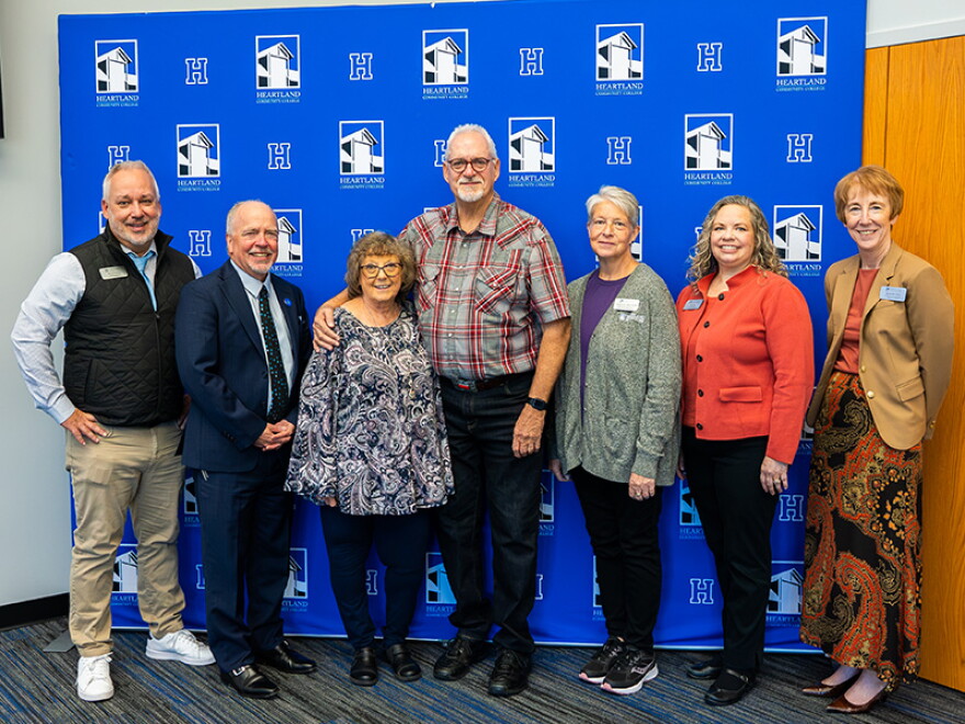 A group of adults, including Keith Cornille and Jim Davis, stand together for a photo in front of a blue backdrop. 
