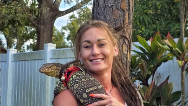 Woman with tattoos holds lizard on chest