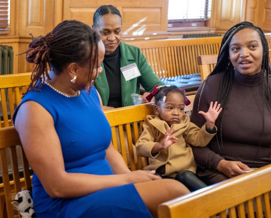 Darasimi Mosley sits between her aunt, Rep. Brooklynne Mosley, D-Lawrence, left, and her mom, Taylor Mosley, before a Jan. 12, 2026 news conference at the Statehouse.