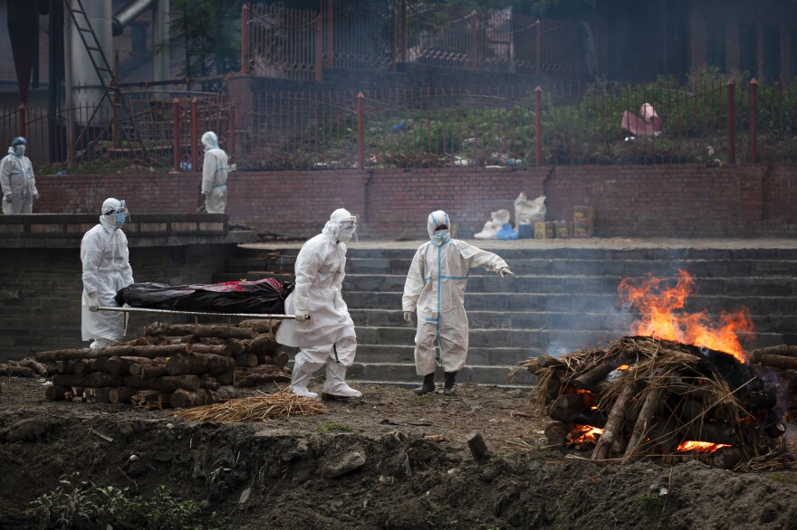 Workers in protective gear carry the body of a person who died of COVID-19 for cremation on the bank of Bagmati River in Kathmandu. As a wave of infections sweeps Nepal, the only crematorium in Kathmandu Valley is struggling to cope with the flow of bodies.