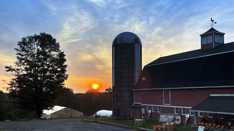 A rising sun elevates just above the tree line and behind Red Barn Creamery and Farm Stand in Mansfield, Connecticut, September 18, 2024.
