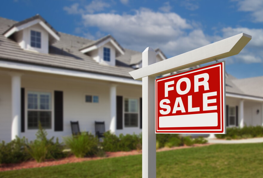 A white apartment buildings with a red sign in front of it that says "For Sale". 