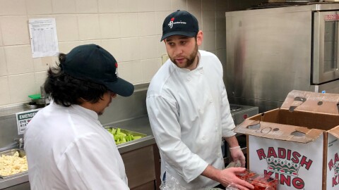 Two chefs standing with fresh produce in a kitchen.