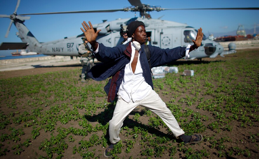 A Haitian man tries to keep a crowd of people from rushing a U.S. Navy helicopter as it touches down to drop off water in downtown Port-au-Prince on Jan. 16, 2010.